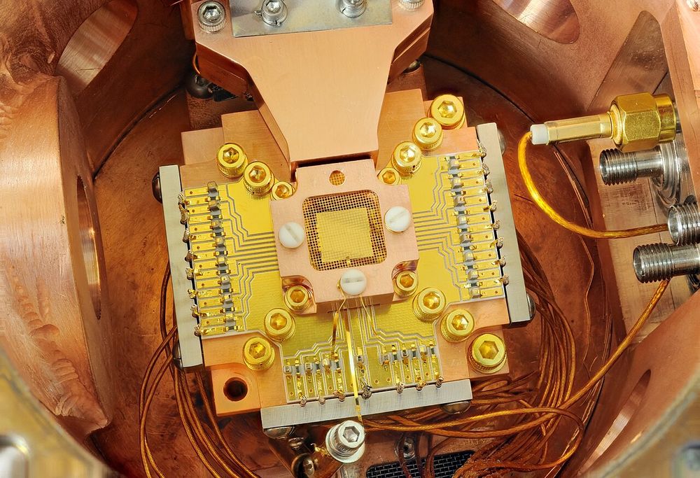 A gold-plated chip inside a copper housing, wired with gold traces and thin cables: an ion trap.